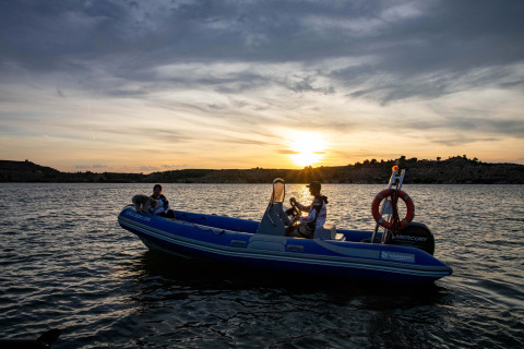Due persone su un gommone al tramonto sul TAIGA Lake Caspe, circondati dal paesaggio collinare di Aragón, Spagna.