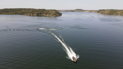 Due barche sfrecciano sull’acqua tranquilla presso il TAIGA Lake Caspe holiday park in Aragona, Spagna, tra colline verdi.