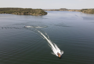 Due barche sfrecciano sull’acqua tranquilla presso il TAIGA Lake Caspe holiday park in Aragona, Spagna, tra colline verdi.
