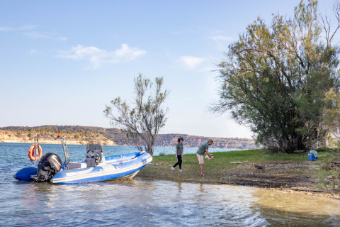 Persone giocano con un cane sulla riva del lago accanto a una barca blu al TAIGA Lake Caspe in Aragona, Spagna.