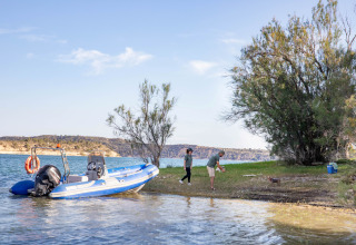 Persone giocano con un cane sulla riva del lago accanto a una barca blu al TAIGA Lake Caspe in Aragona, Spagna.