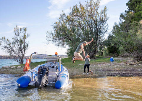 Uomo salta dalla barca alla riva al TAIGA Lake Caspe in Aragona, Spagna, donna e cane osservano.
