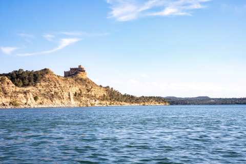 Vista su TAIGA Lake Caspe in Aragona, Spagna, con un castello in cima a una collina sotto il cielo azzurro.