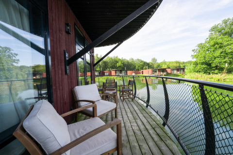 Knus lodgebalkon met comfortabele stoelen, uitzicht op een vijver en meer lodges verderop in het groen.
