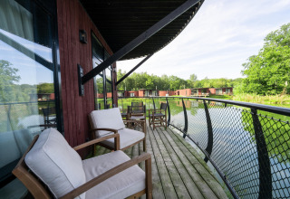 Knus lodgebalkon met comfortabele stoelen, uitzicht op een vijver en meer lodges verderop in het groen.