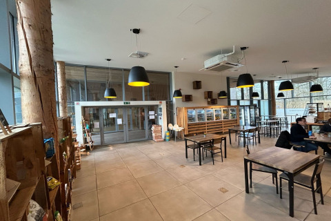 Bright, modern café area at a glamping accommodation with wood tables, large windows, and pendant lights.