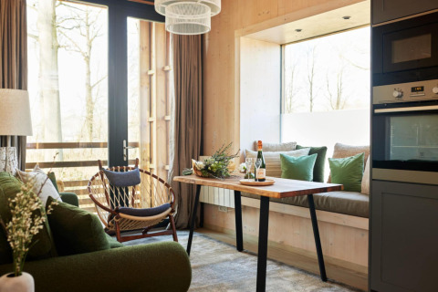 Accogliente soggiorno a The Blue Lodge by YourNature, Belgio, con divano verde, tavolo in legno e finestrone.