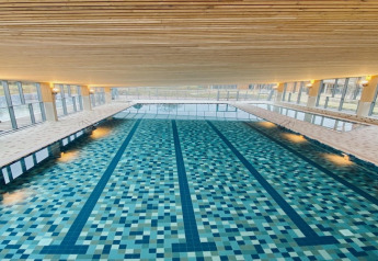 Piscina coperta con piastrelle a mosaico e grandi finestre a The Blue Lodge by YourNature in Belgio.