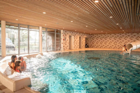 Piscina coperta con famiglia che si rilassa e bimbo sullo scivolo, The Blue Lodge, Belgio.