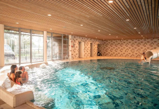 Piscina coperta con famiglia che si rilassa e bimbo sullo scivolo, The Blue Lodge, Belgio.