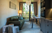 Petit salon moderne d'une tiny house, canapé vert, table à manger, grande baie vitrée donnant sur la nature.