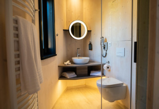 Bagno moderno in The Blue Lodge by YourNature, Belgio, con specchio circolare e WC sospeso.
