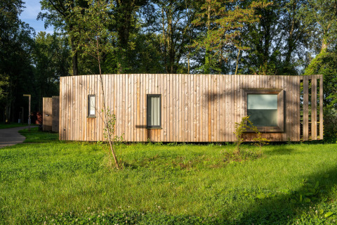 Moderne glampingindkvartering med træfacade i naturskønne omgivelser med grøn græsplæne og træer.
