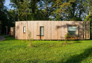Moderne glampingindkvartering med træfacade i naturskønne omgivelser med grøn græsplæne og træer.