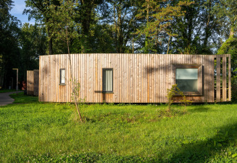 Hébergement glamping moderne à façade boisée, installé au milieu d’une pelouse verte et d’arbres.