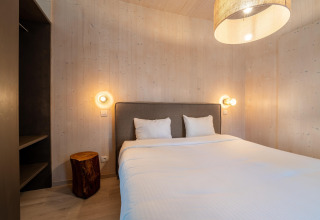 Camera da letto in una tiny house con letto matrimoniale, pareti in legno e luce soffusa accogliente.