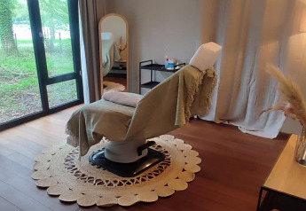 Accogliente sala trattamenti a The Blue Lodge by YourNature, Belgio, con ampia poltrona e vista sul bosco.