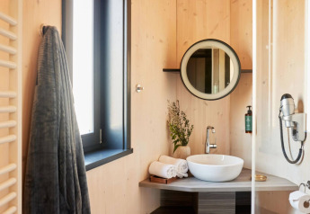 Salle de bain moderne au Blue Lodge, vasque ronde, miroir, serviettes et fenêtre dans une tiny house en Belgique.