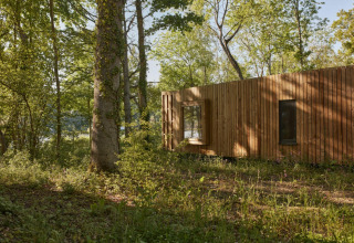 La tiny house The Blue Lodge by YourNature in Belgio, circondata da una foresta verde e luminosa.