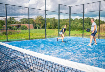 Deux personnes jouent au padel sur un terrain bleu à The Blue Lodge by YourNature en Belgique, entourés de verdure.