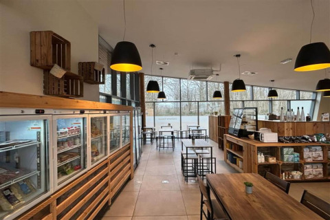 Caffetteria luminosa in un glamping con arredi in legno, grandi finestre, freezer e lampade nere.