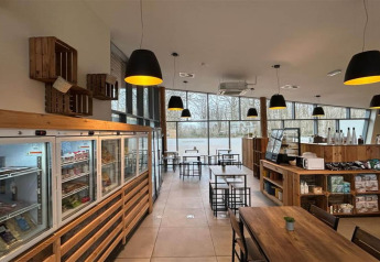 Caffetteria luminosa in un glamping con arredi in legno, grandi finestre, freezer e lampade nere.
