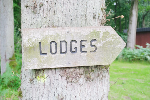 Cartello di legno con la scritta 'LODGES' presso The Blue Lodge by YourNature, Belgio, in mezzo al verde.