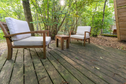 Holzterrasse mit zwei weißen Sesseln und einem kleinen Tisch im grünen Wald bei The Cottage by YourNature.