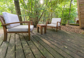 Holzterrasse mit zwei weißen Sesseln und einem kleinen Tisch im grünen Wald bei The Cottage by YourNature.