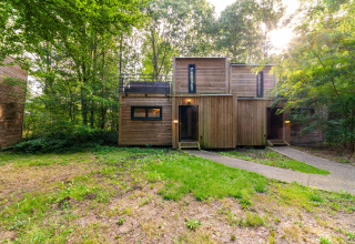 Moderna cabaña de madera en el bosque, alojamiento glamping The Cottage por YourNature, luz de atardecer.