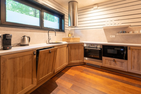 Moderne keuken bij The Cottage by YourNature glamping met houten kasten, oven, magnetron en raam.