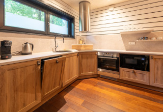 Moderne keuken bij The Cottage by YourNature glamping met houten kasten, oven, magnetron en raam.