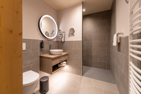 Moderne badkamer met ronde spiegel, houten accenten en inloopdouche bij The Cottage by YourNature.