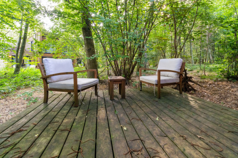 Zwei gemütliche Stühle auf einer Holzterrasse im Wald bei The Cottage by YourNature Glamping, umgeben von Bäumen.