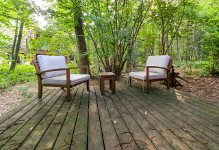 Zwei gemütliche Stühle auf einer Holzterrasse im Wald bei The Cottage by YourNature Glamping, umgeben von Bäumen.
