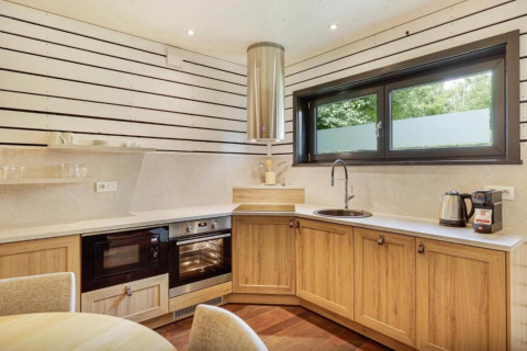 Moderne glampingkeuken bij The Cottage by YourNature met houten kasten, oven, magnetron en groot raam.