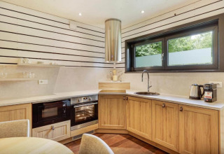 Moderne glampingkeuken bij The Cottage by YourNature met houten kasten, oven, magnetron en groot raam.