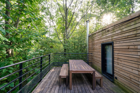 Houten terras met tafel en banken tussen bomen bij The Cottage by YourNature glamping accommodatie.