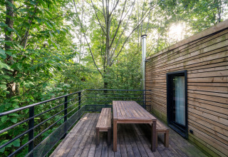 Terraza de madera con mesa y bancos rodeada de árboles en The Cottage by YourNature, un glamping.