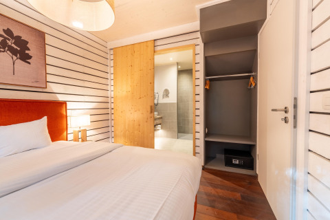 Schlafzimmer im The Cottage von YourNature mit offenem Kleiderschrank, Safe und Holztür zum Bad.