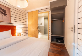 Schlafzimmer im The Cottage von YourNature mit offenem Kleiderschrank, Safe und Holztür zum Bad.