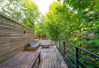 Holzterrasse mit Sitzbänken und Tisch im Grünen, The Cottage by YourNature in Belgien.