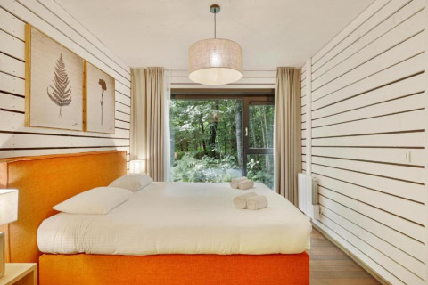 Dormitorio en The Cottage by YourNature con cama naranja, paredes blancas y vista al bosque exterior.