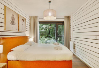 Dormitorio en The Cottage by YourNature con cama naranja, paredes blancas y vista al bosque exterior.