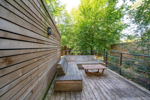 Udendørs træterrasse med bænk og bord ved The Cottage by YourNature, omgivet af skov i Belgien.