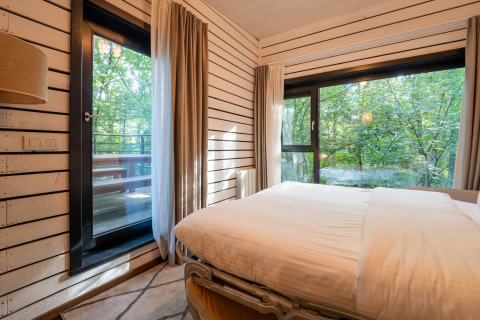 Slaapkamer in The Cottage by YourNature in België met grote ramen en uitzicht op bos en veranda.