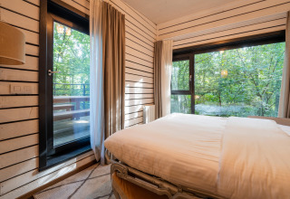 Slaapkamer in The Cottage by YourNature in België met grote ramen en uitzicht op bos en veranda.