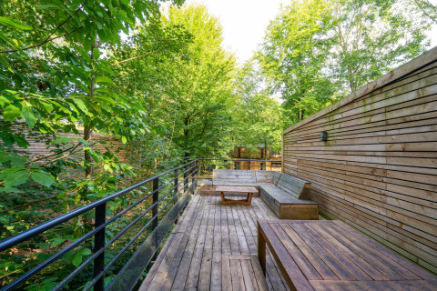 Terraza de madera con banco y mesa, rodeada de árboles en Nature house The Cottage by YourNature en Bélgica.