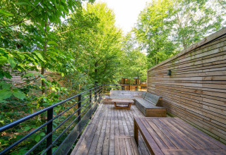 Terraza de madera con banco y mesa, rodeada de árboles en Nature house The Cottage by YourNature en Bélgica.
