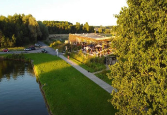 Aerial view of a glamping site with a lake, greenery, walking path, and people relaxing at the terrace.